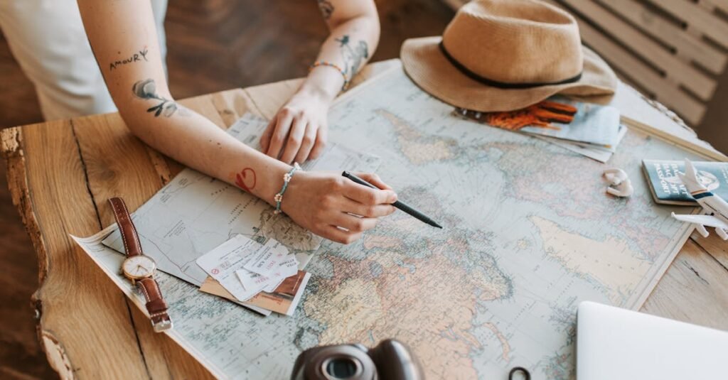 Tattooed woman planning a trip with a world map, passports, and travel essentials on a wooden table.
